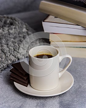 A white mug with coffee on a saucer on a gray background with books.