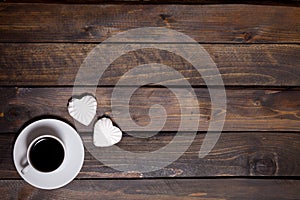 White mug of coffee and two marshmallows in the shape of hearts on a wooden background