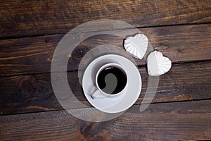 White mug of coffee and two marshmallows in the shape of hearts on a wooden background for breakfast