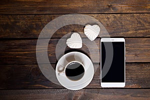 White mug of coffee and two marshmallows in the shape of hearts on a wooden background for breakfast