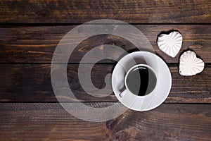 White mug of coffee and two marshmallows in the shape of hearts on a wooden background for breakfast