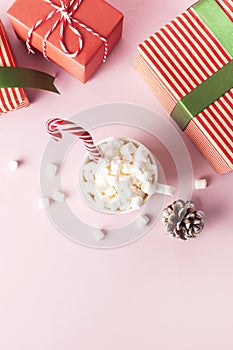 White mug with marshmallows Candy Cane gifts boxes with green ribbon on pink background Flat Lay Winter traditional drink food