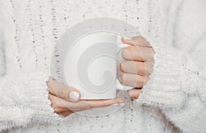 White mug mockup. Girl is holding white 11 oz ceramic cup in hands, wears cozy knitted sweater. Front view, copy space