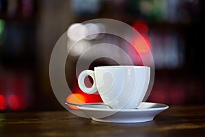 a white mug with a saucer and a spoon is on a wooden table in a restaurant. Close-up