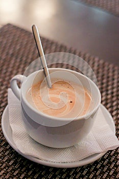 White mug with a spoon and hot cappuccino stands on a saucer. A small Cup on a saucer with a napkin. Dark stand on the table