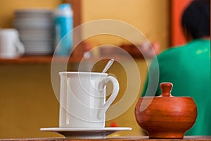White mug and wooden suger-bowl at table on cafe background