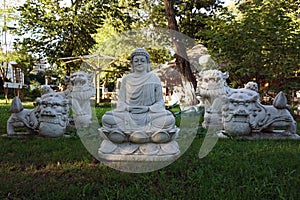 White murble buddha sculpture meditating, with asian lions in a garden with green grass at sunset time.