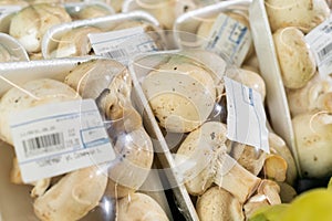 White mushrooms wrapped in plastic package lying on market stall for sale