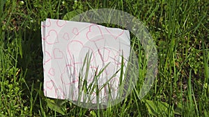 A white napkin with red hearts lies on fresh green grass. Spring love concept. Valentine`s Day symbolic. April nature wakes up. Bl