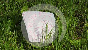 A white napkin with red hearts lies on fresh green grass. Spring love concept. Valentine`s Day symbolic. April nature wakes up. Bl