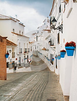 White narrow streets with whitewashed traditional andalusian houses, blue pots with red geranium at the walls at little touristic