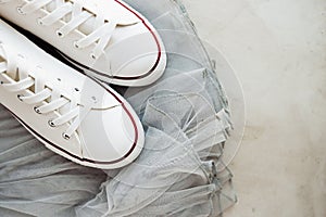 White new clean sneakers with white laces on a rubber sole on a gray tulle fabric. a combination of sports shoes and formal wear.