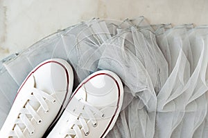 White new clean sneakers with white laces on a rubber sole on a gray tulle fabric. a combination of sports shoes and formal wear.