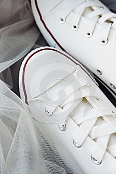 White new clean sneakers with white laces on a rubber sole on a gray tulle fabric. a combination of sports shoes and formal wear.