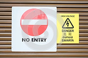 A white no entry and a yellow high voltage warning signs