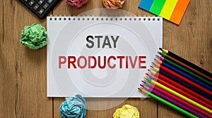 White note with inscription `stay productive` on beautiful wooden table, colored paper, colored pencils, and calculator. Busines