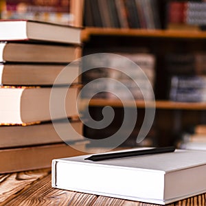 A white notebook and a black pencil on the desktop with bookshelves in the background. Books