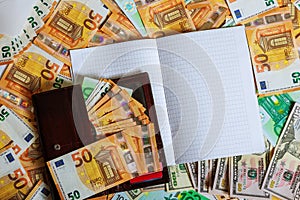 A white notebook with blank pages lay on a set of banknotes of 100 euros, 50 euros and 100 dollars.