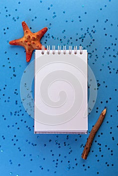 White notebook on blue background with stars glitters, pencil and starfish