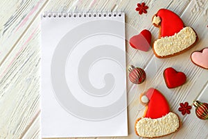 White notebook for Christmas wishes, goals, recipes for the New Year 2021 among gingerbread cookies in form of Santa Claus hat,