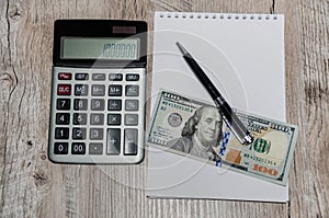 White notebook, dollars, calculator and pen on a wooden table