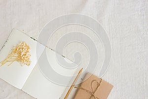 White notebook with flowers and gift box over the white fabric.