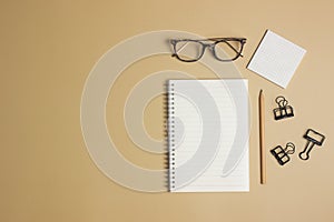 White notebook with glasses, pencil and black clip over the brown background.