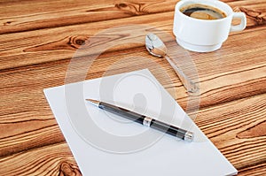 White notebook with pen and cup of coffee on wooden background.