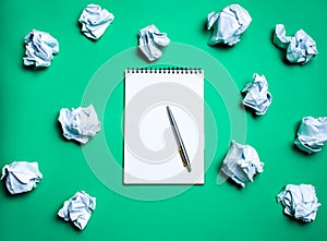 white notebook with pen on a green background among paper balls. The concept of generating ideas, inventing new ideas. Paper balls