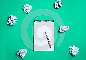 White notebook with pen on a green background among paper balls. The concept of generating ideas, inventing new ideas. Paper balls photo