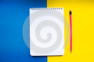 White notebook with pink pencil on a yellow-blue background