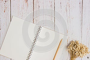 White notebook with wooden pencil and white flowers on wooden table.