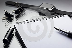 White notepad on it black pen near a smart clock closeup on a glossy desk, concept