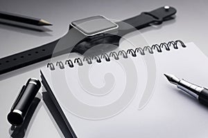 White notepad on it black pen near a smart clock and pencil closeup on a glossy desk, concept