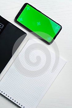 White notepad laptop and green screen smartphone on white tables, copy space, flat lay, top view, mock up