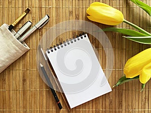 white notepad on a mat with tassels, pens and yellow tulips