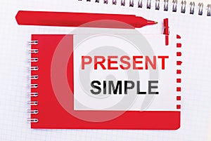 On a white notepad, a red pen, a red notepad and a white sheet of paper with the text PRESENT SIMPLE