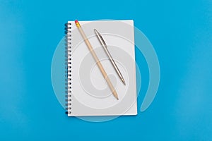 White notepad with steel pen on a blue background. Office table, minimal composition. Copy space