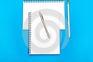 White notepad with steel pen on a blue background. Office table, minimal composition. Copy space