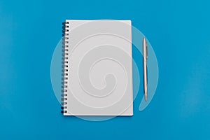 White notepad with steel pen on a blue background. Office table, minimal composition. Copy space