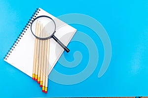 White notepad with steel pen on a blue background. Office table, minimal composition. Magnifying glass. Copy space