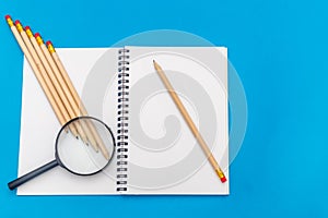 White notepad with steel pen on a blue background. Office table, minimal composition. Magnifying glass. Copy space