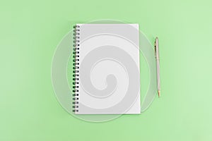 White notepad with steel pen on a green background. Office table, minimal composition. Copy space