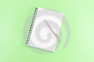 White notepad with steel pen on a green background. Office table, minimal composition. Copy space