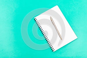 White notepad with steel pen on a green background. Office table, minimal composition. Copy space