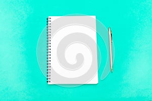 White notepad with steel pen on a green background. Office table, minimal composition. Copy space