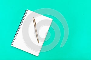 White notepad with steel pen on a green background. Office table, minimal composition. Copy space