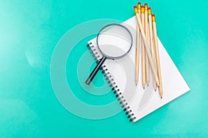 White notepad with steel pen on a green background. Office table, minimal composition. Magnifying glass. Copy space