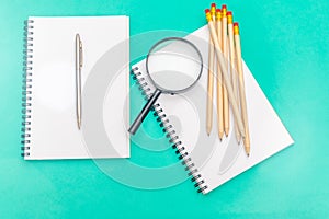 White notepad with steel pen on a green background. Office table, minimal composition. Magnifying glass. Copy space