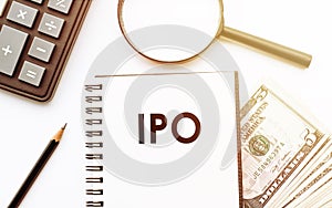 White notepad with the text of the IPO - Initial public offering, on the background of dollars and office tools